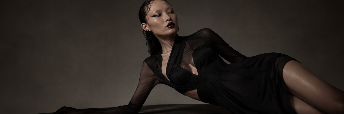 Modella in abito nero fra schizzi, tessuti e strumenti sartoriali